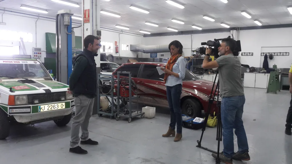 Un equipo de televisión graba en el taller de Automoción, con el Fiat Panda del proyecto al fondo